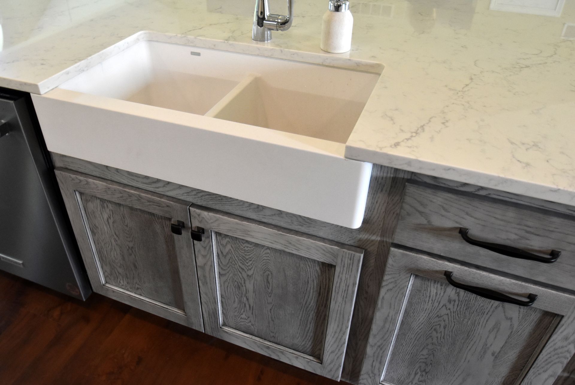 Modern kitchen sink with white countertop and gray cabinets, plus a dark appliance on the left