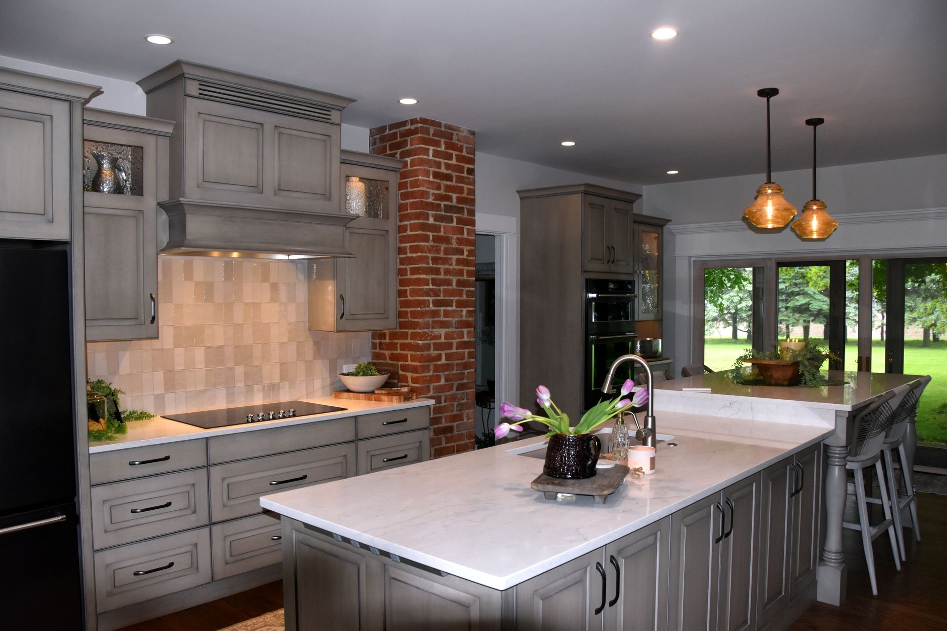 Modern kitchen with gray cabinets, marble island, pendant lights, and a dining area by large windows
