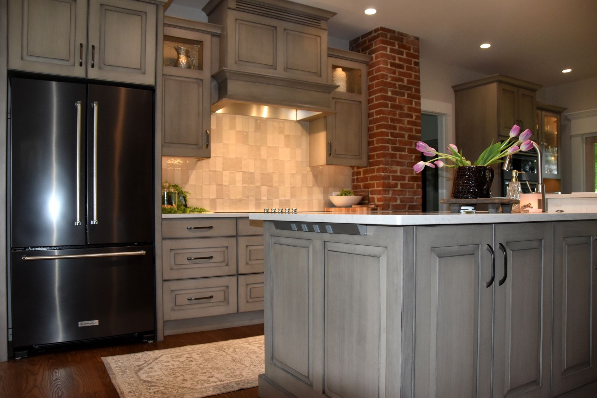 Modern kitchen with gray cabinets, black refrigerator, brick backsplash, and island with flowers