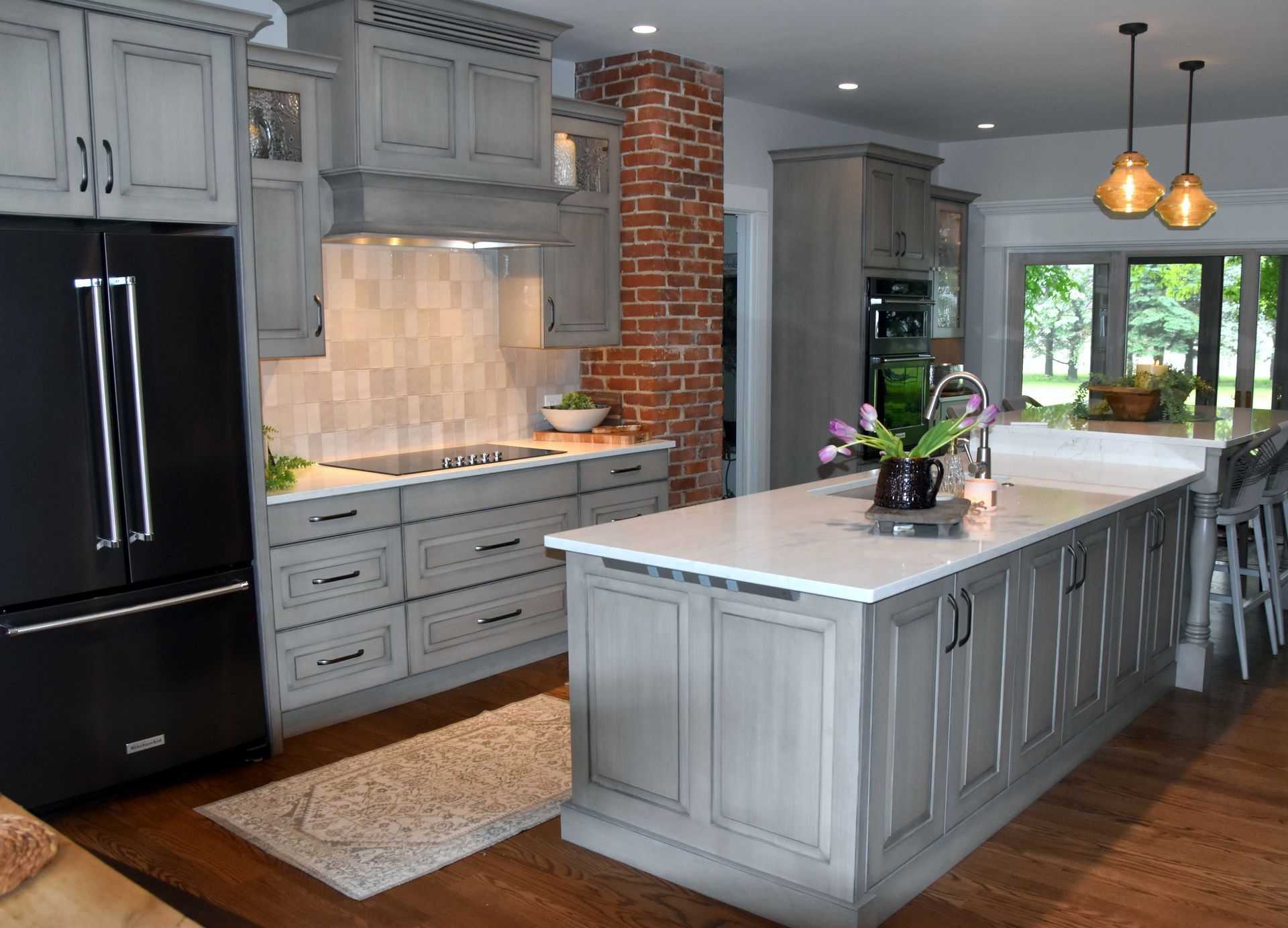 Modern gray kitchen with black appliances, white island, brick accent wall, and pendant lights