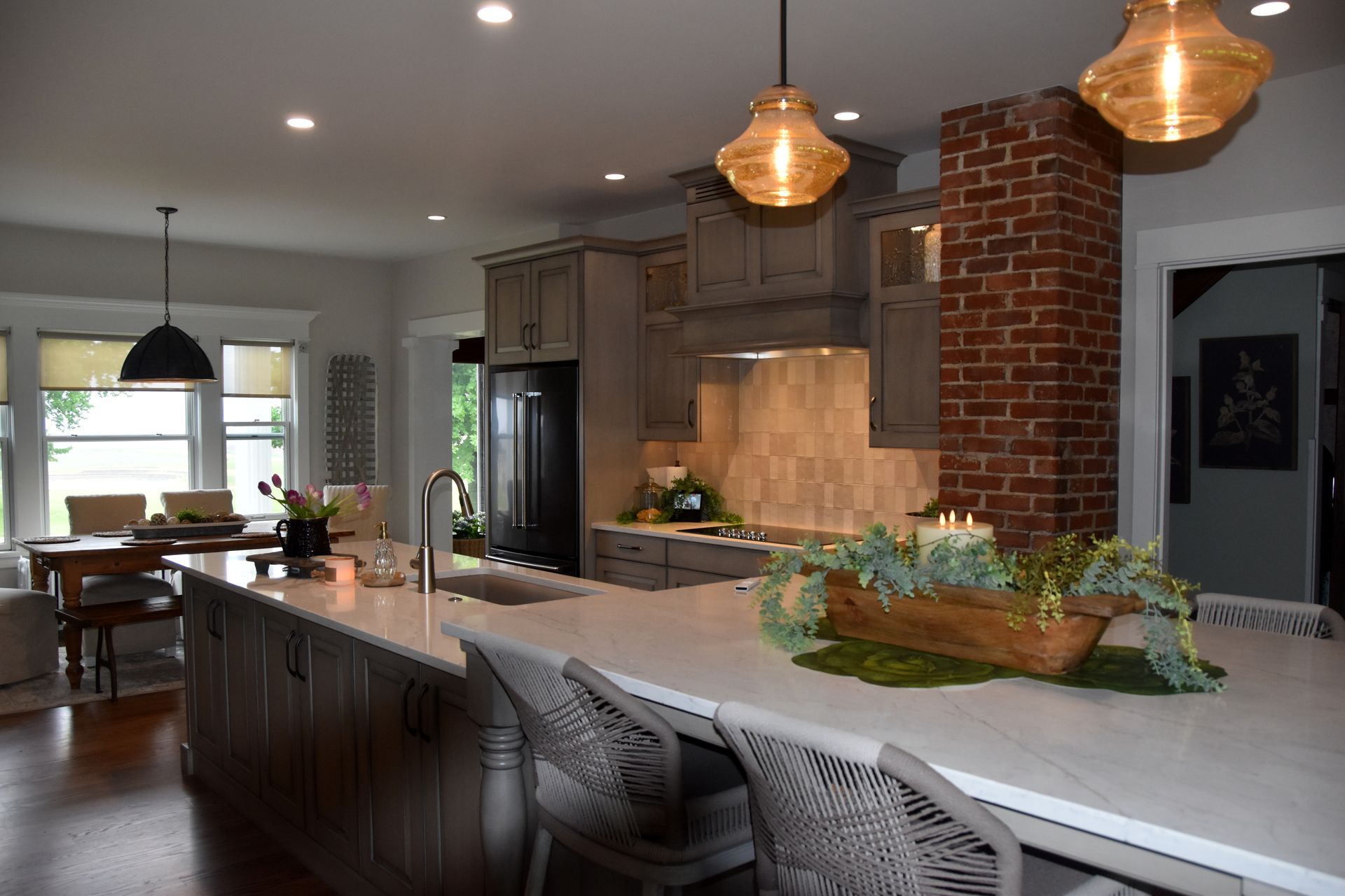 Modern kitchen with large island, brick column, pendant lights, and dining area beyond