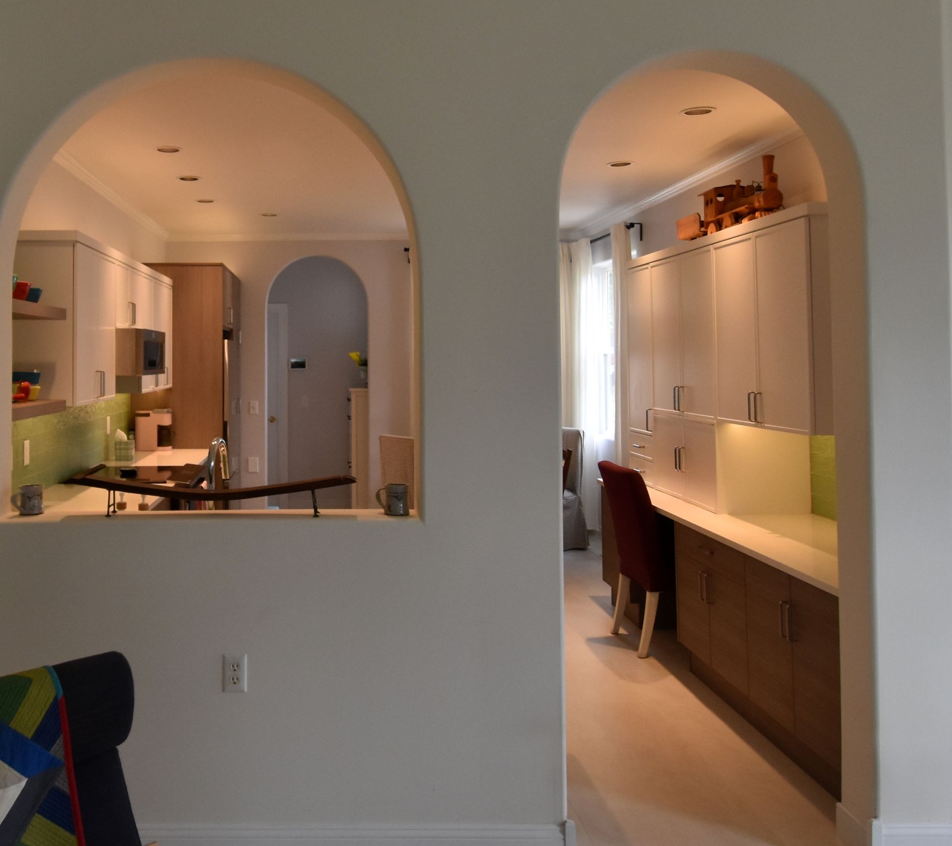 Open-plan kitchen with arched pass-throughs, white walls, wood cabinets, and a lit hallway bar area.