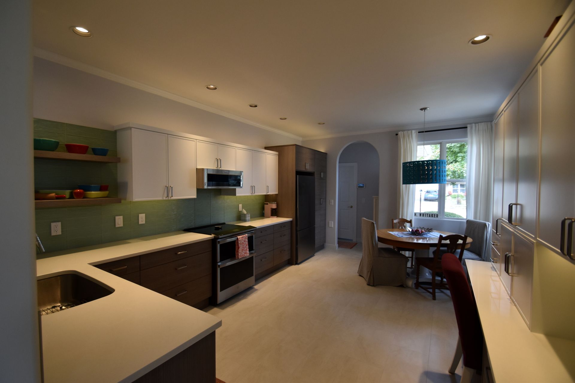Modern kitchen and dining area with white cabinets, black countertops, and a table by a bright window.