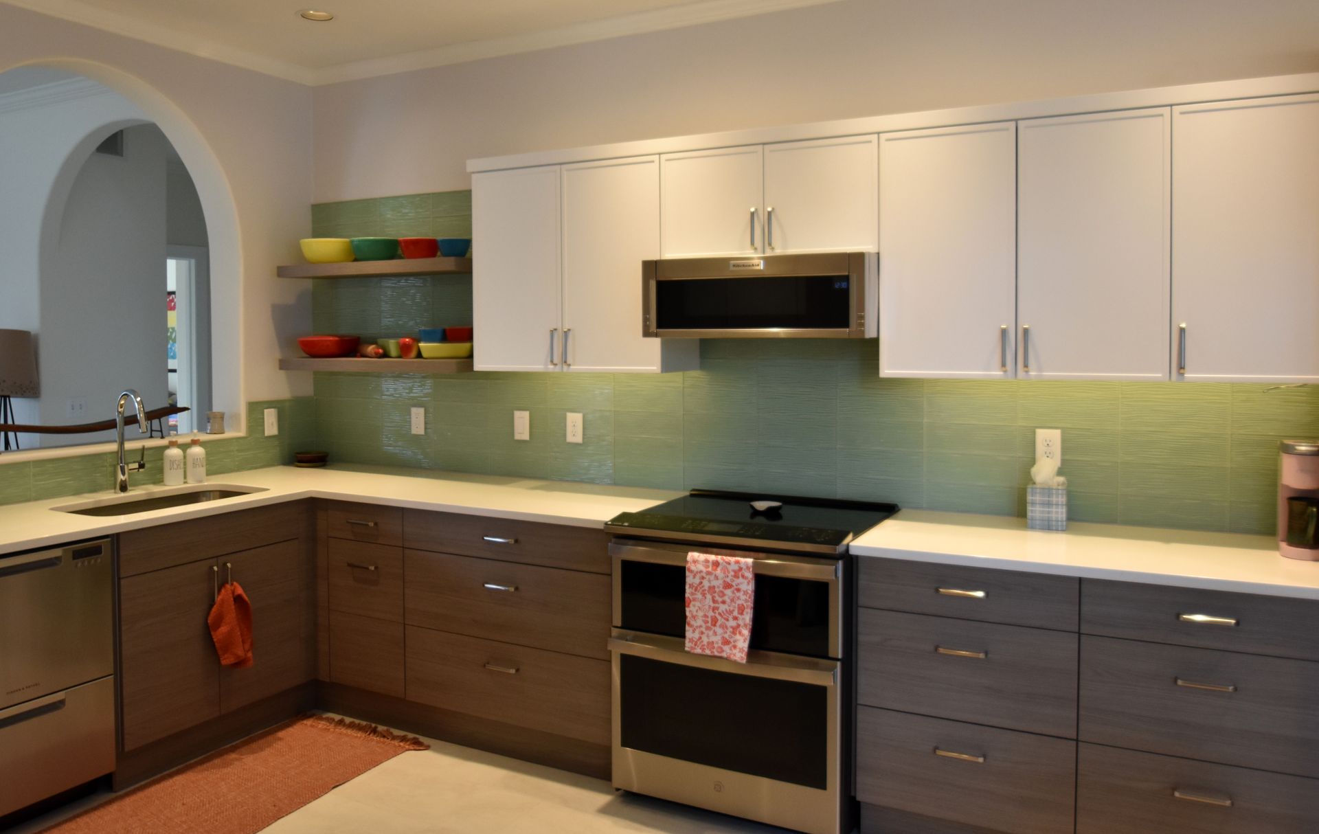 Modern kitchen with white and brown cabinets, green tile backsplash, stainless appliances, and an arched pass-through