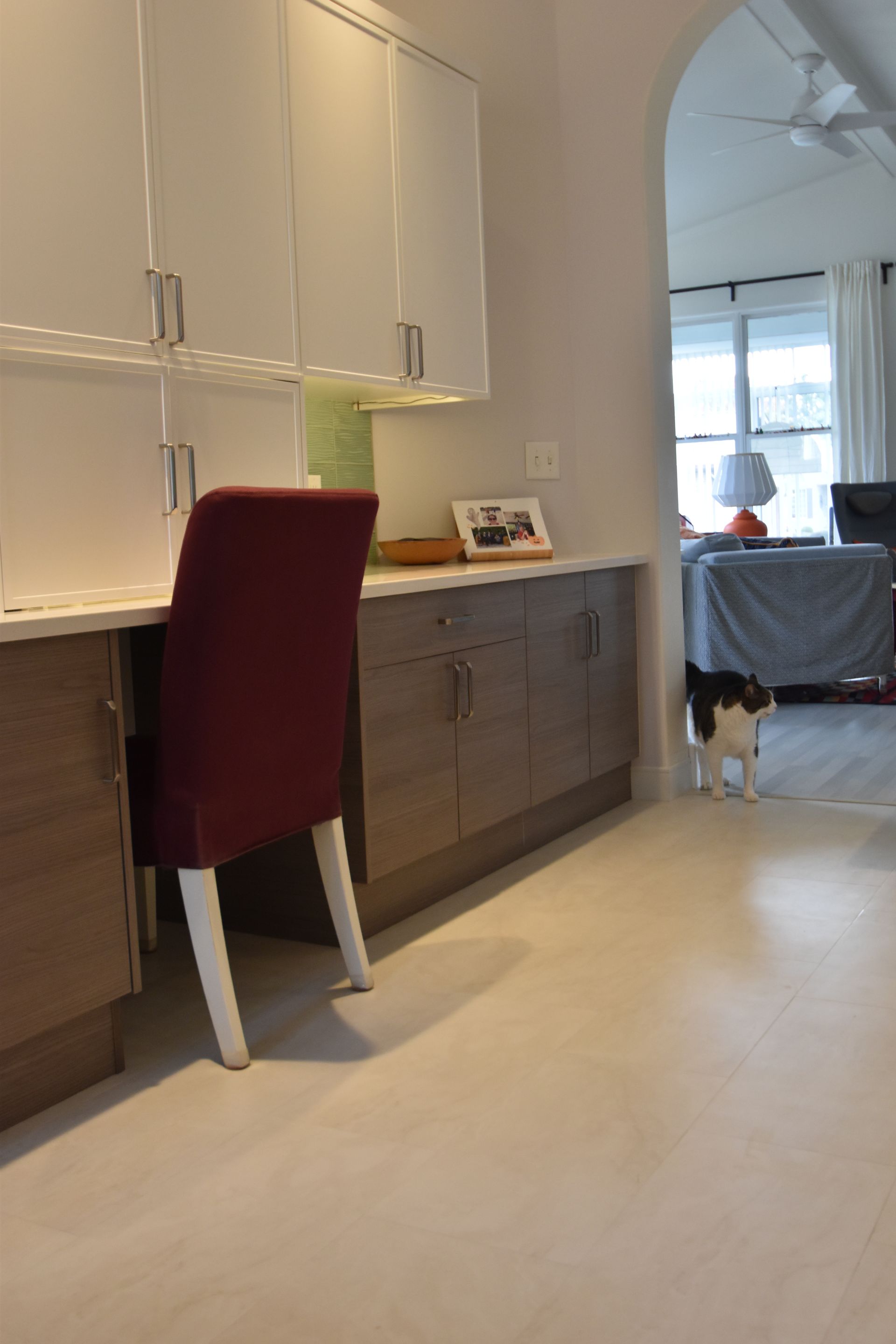 Modern kitchen with white cabinets, dark sideboard, red chair, and a small dog near a living room doorway