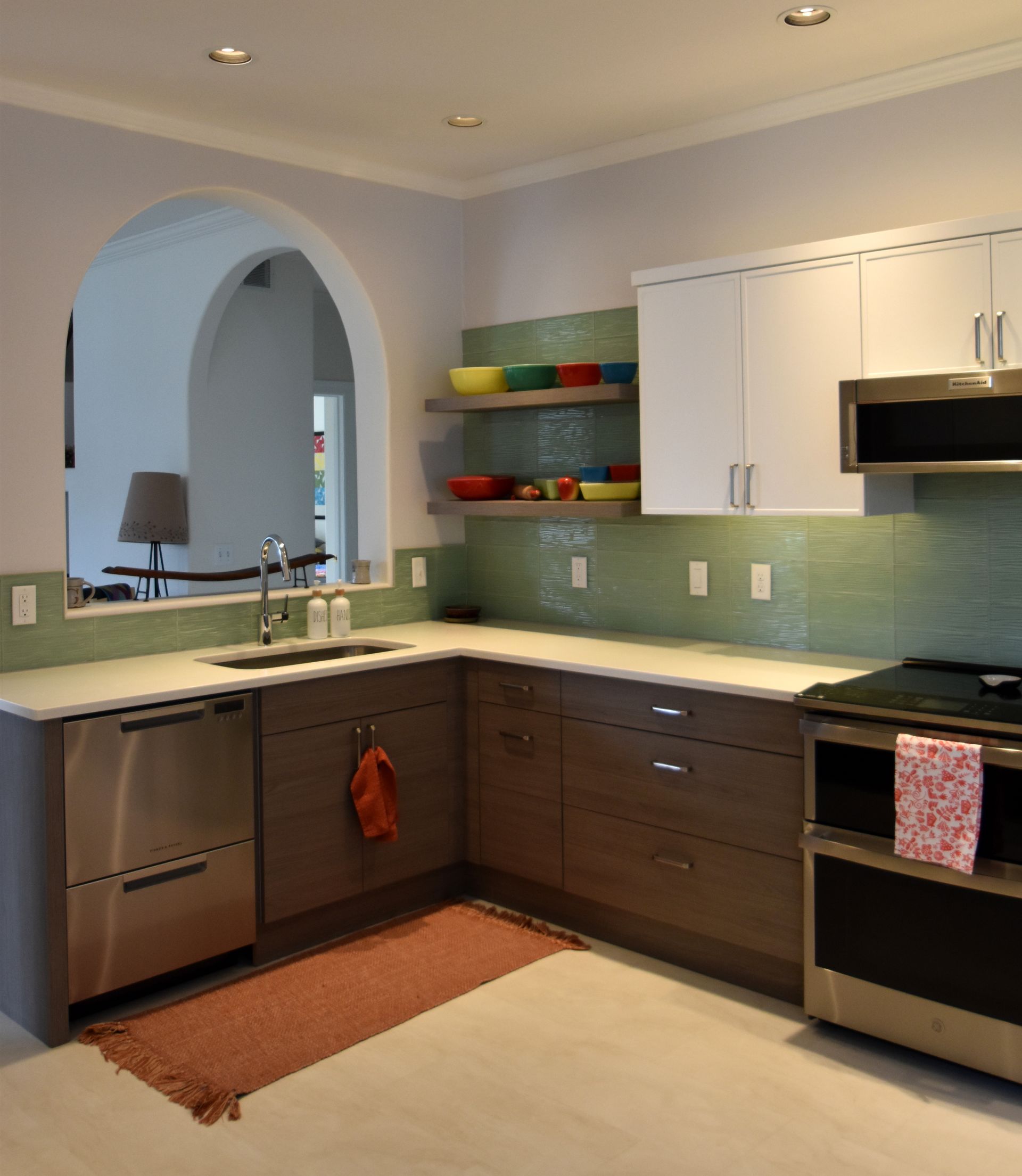 Modern kitchen with white cabinets, gray counters, stainless dishwasher, and a sink under an arched pass-through window