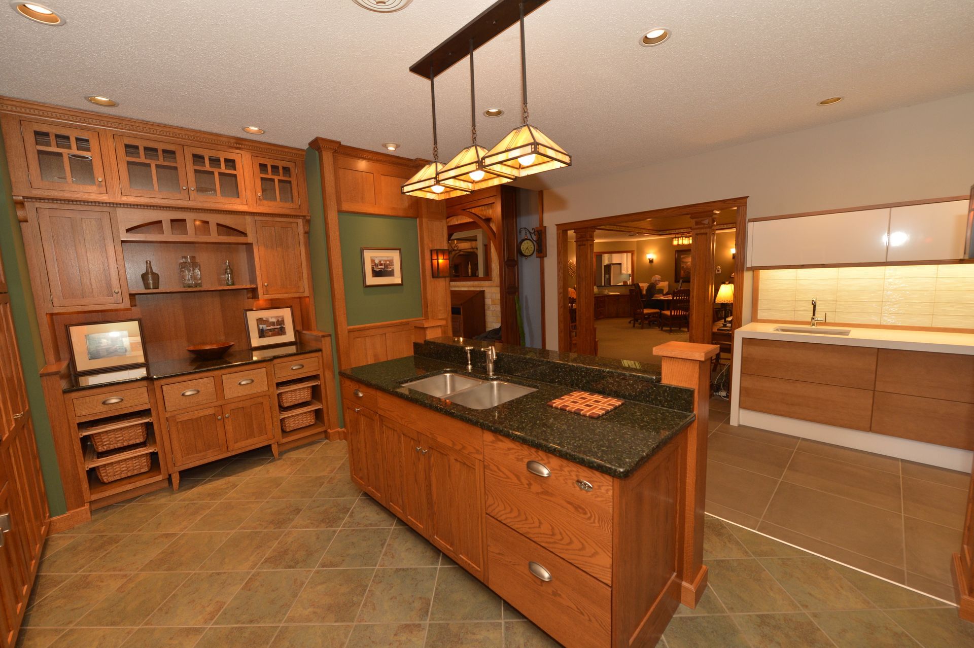 Warm-toned kitchen with wood cabinets, central island, hanging lights, and tiled floor