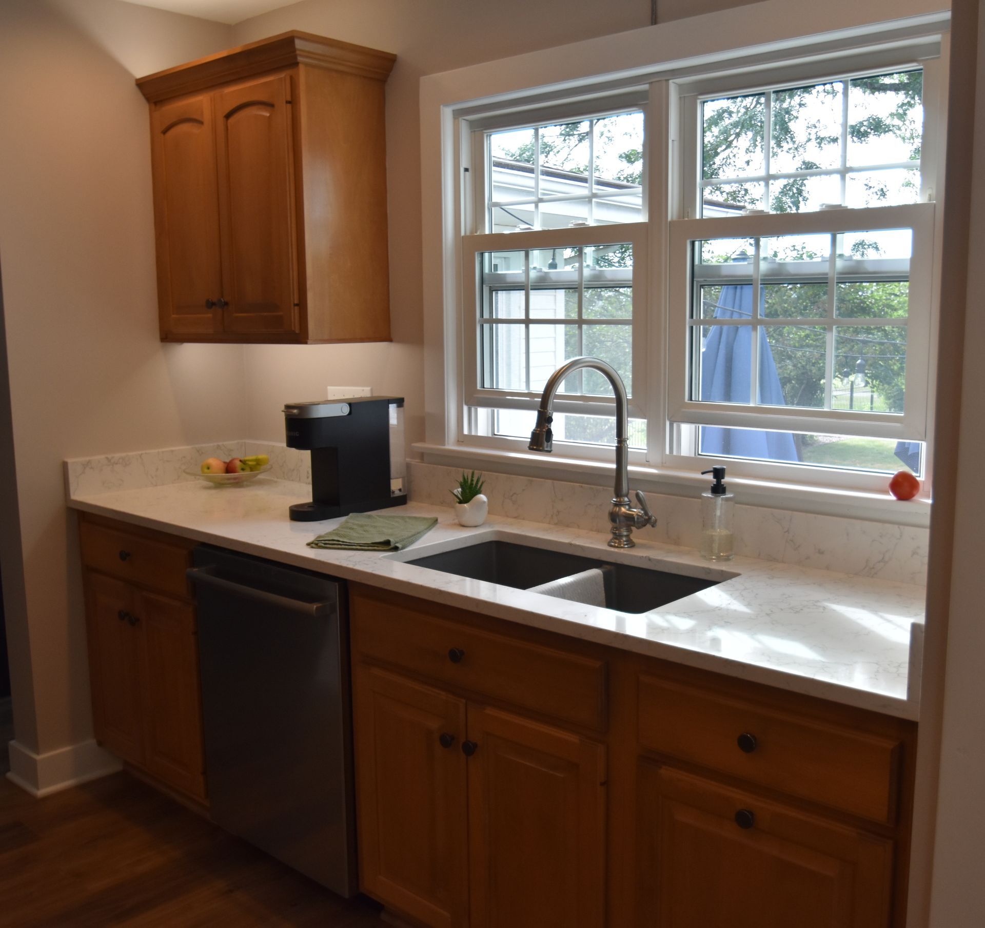 Bright kitchen with wood cabinets, white countertop, sink under a window, and a coffee maker on the counter
