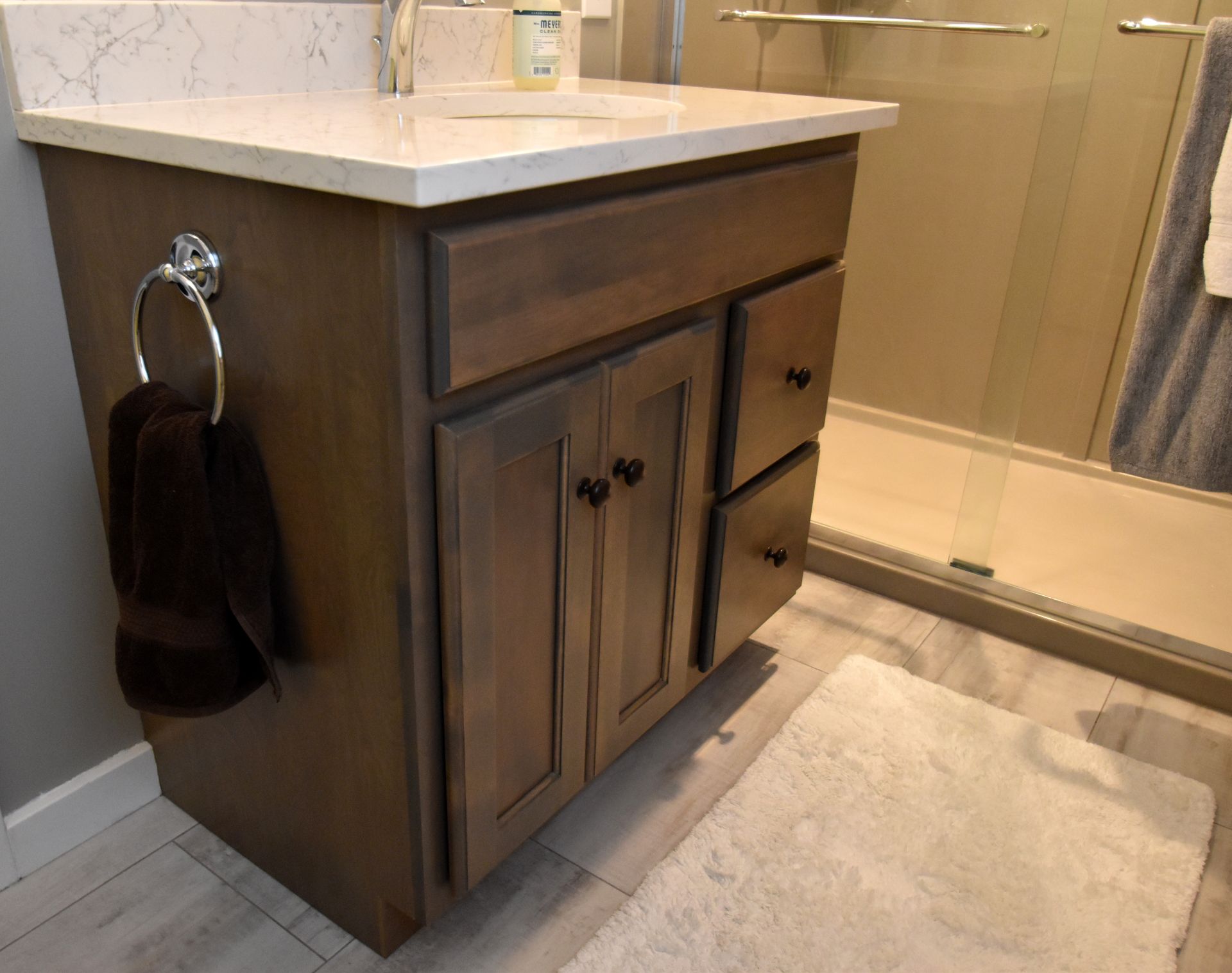 Dark wood bathroom vanity with white countertop and built-in towel ring beside a glass shower