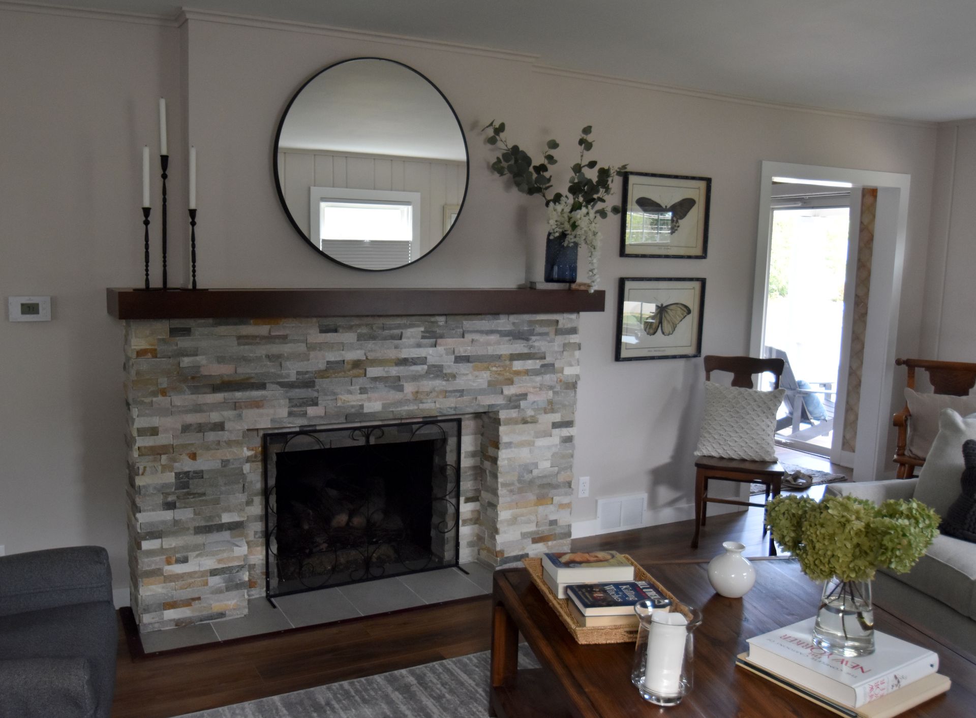 Living room with stone fireplace, round mirror, and coffee table with flowers and candles