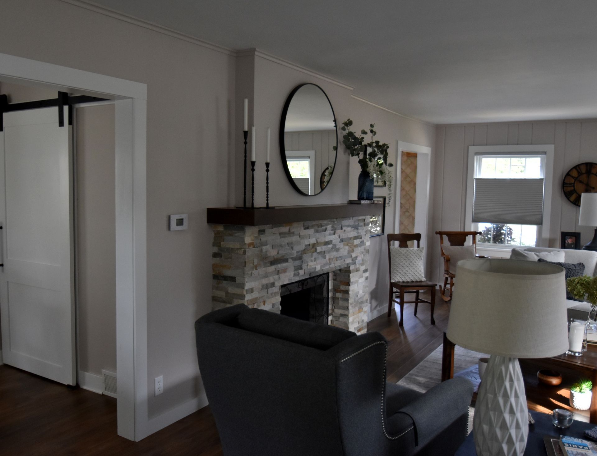 Living room with stone fireplace, black chair, lamp, and a view into the dining area