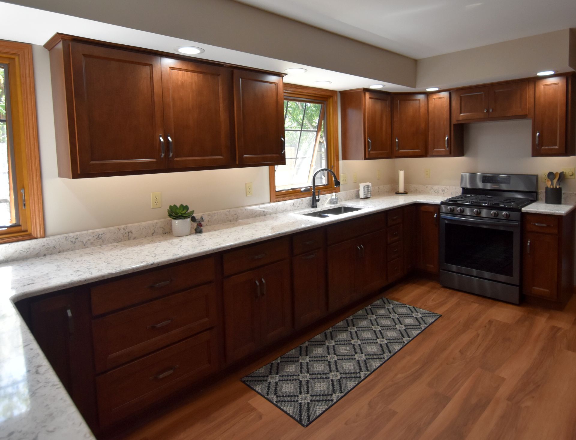 Modern kitchen with dark wood cabinets, white countertops, hardwood floor, and a stove by the window.