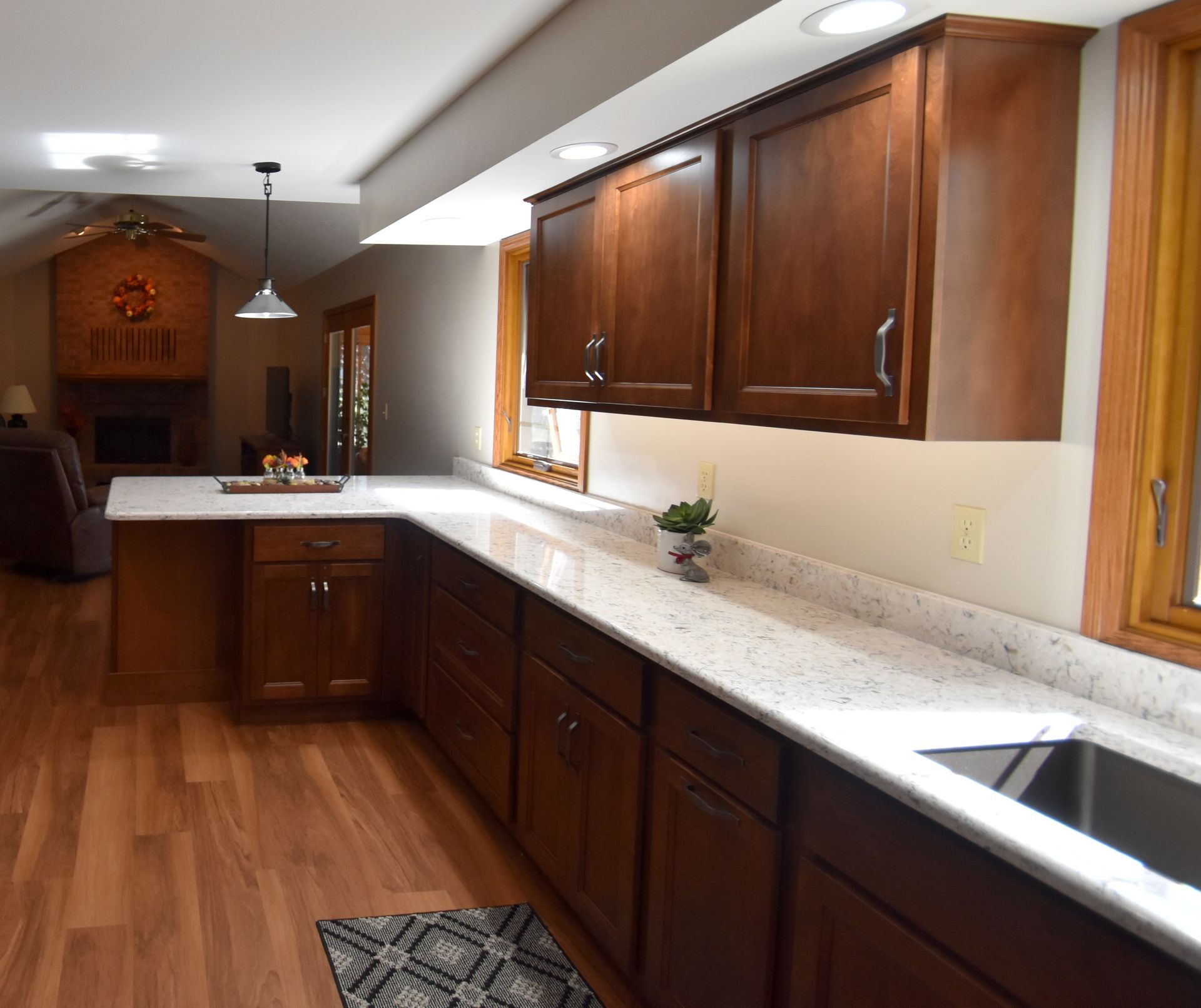 Modern kitchen with dark wood cabinets, white counters, wood floors, and a sink by the window.