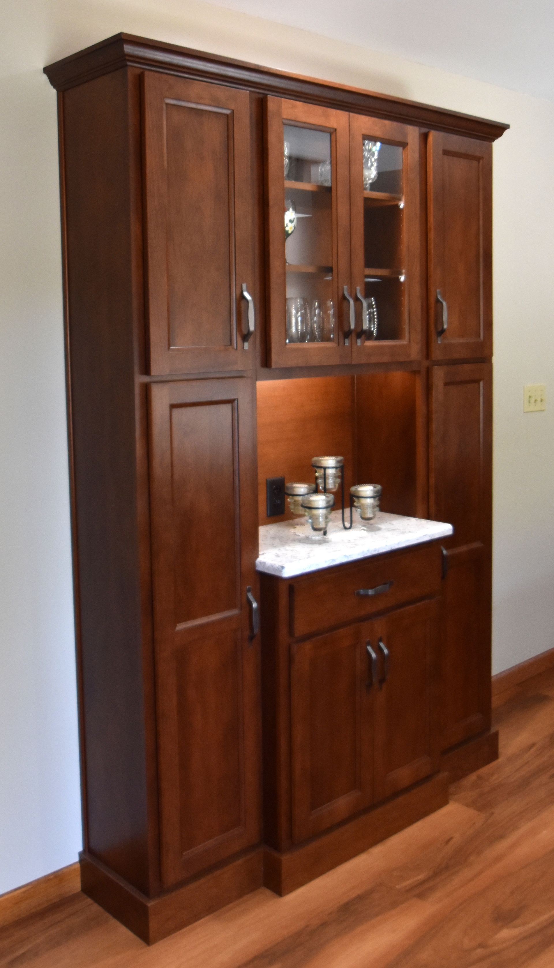 Wooden kitchen cabinet with glass doors and a white countertop against a wall.