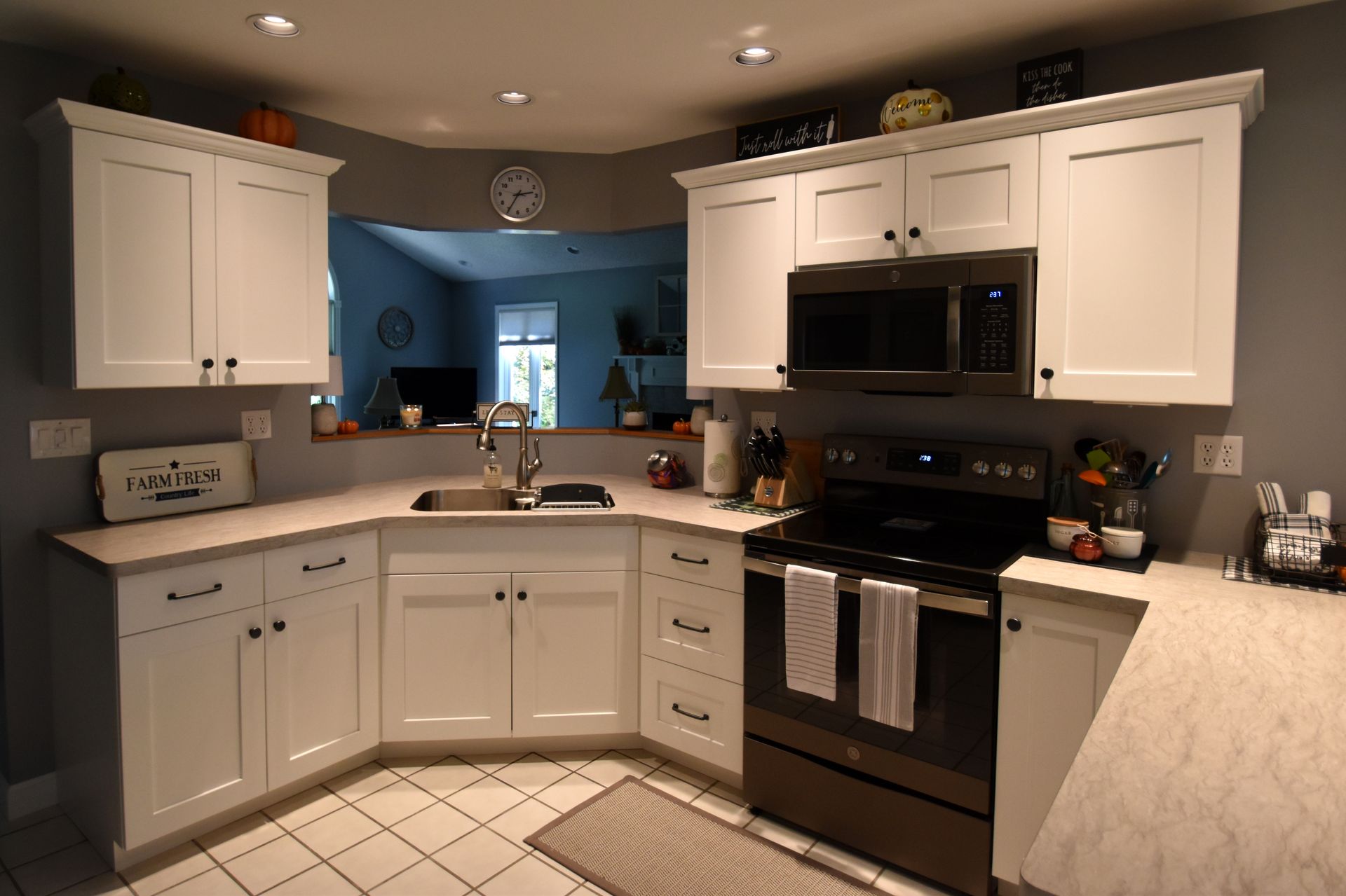 Bright kitchen with white cabinets, black stove and microwave, and tiled floor.