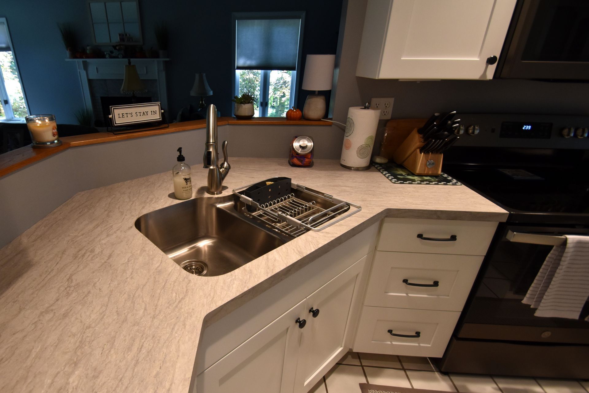 Kitchen island with stainless sink, light countertop, white cabinets, and a black stove nearby.