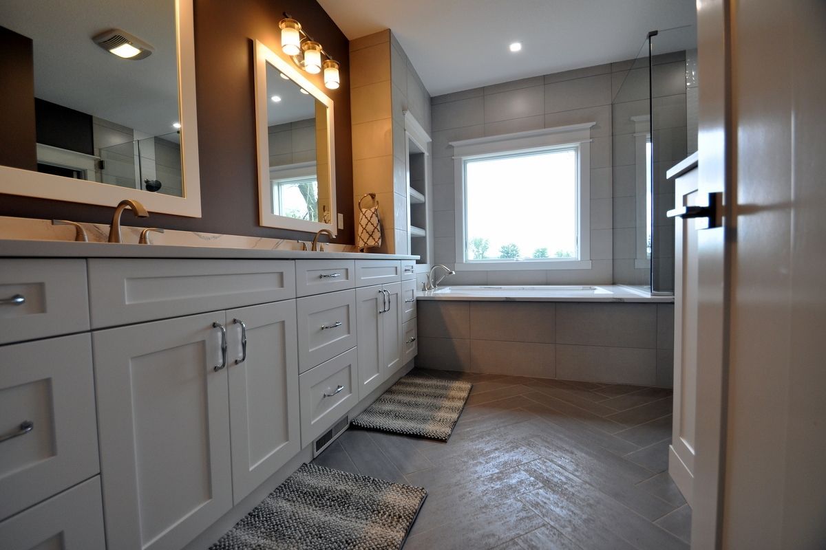 Modern bathroom with white vanity, large mirror, and a window above a built-in soaking tub.