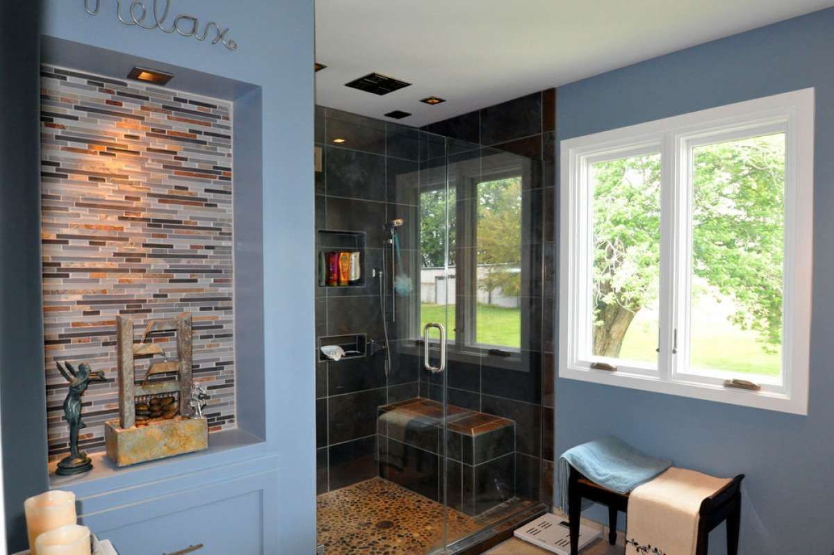 Modern bathroom with dark tile shower, pebble floor, and a window above a bench seat