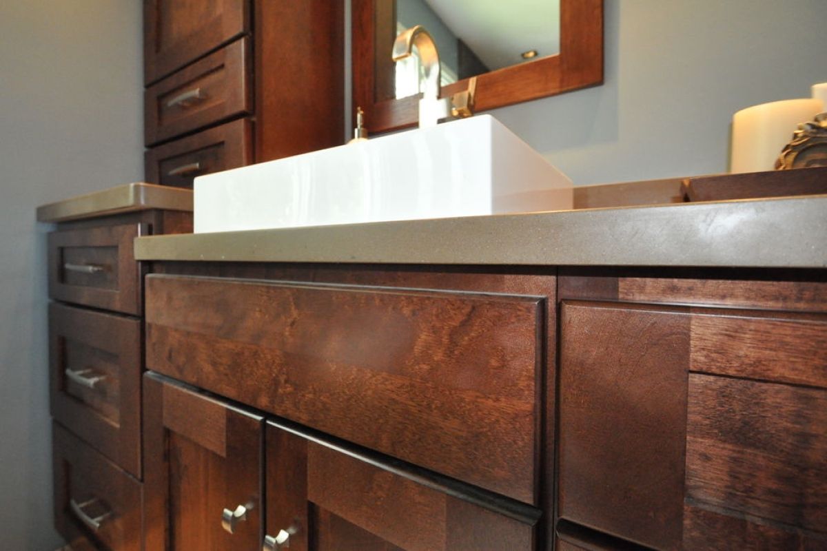 Wooden bathroom vanity with white countertop and sink beneath a mirror