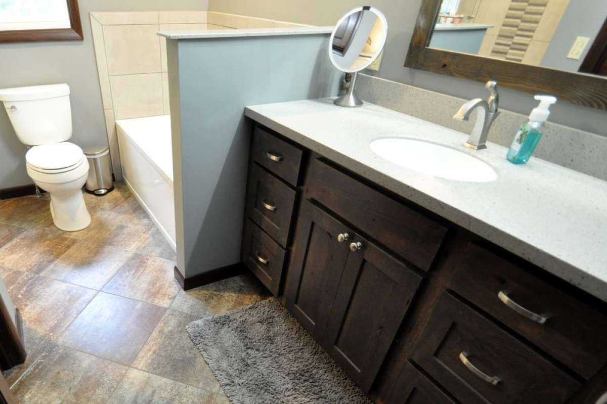 Bathroom vanity with dark cabinets, white countertop, sink, and toilet, shown from a doorway