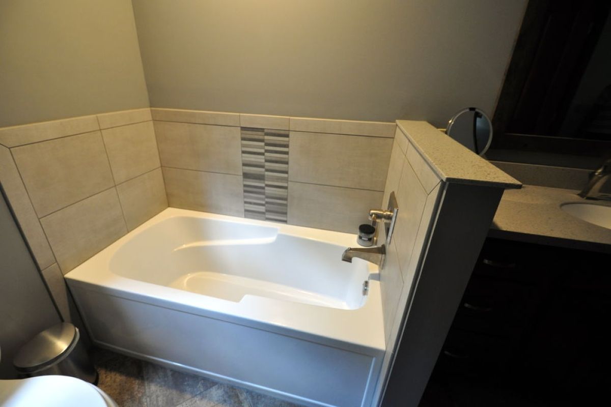Walk-in bathtub with beige tile surround and chrome fixtures in a bathroom.