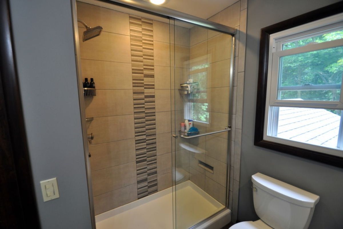 Small bathroom with glass walk-in shower, beige tile, gray wall, and toilet in foreground