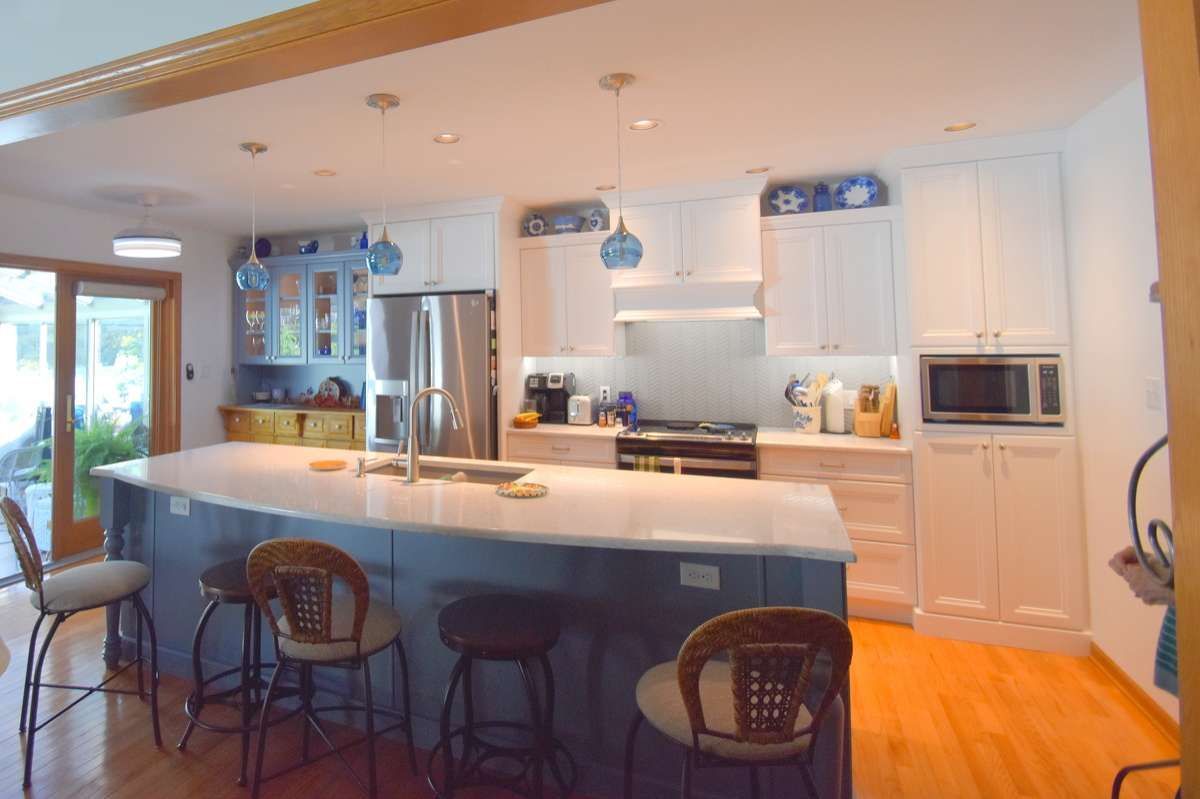 Bright modern kitchen with blue island, white cabinets, stainless fridge, and barstools