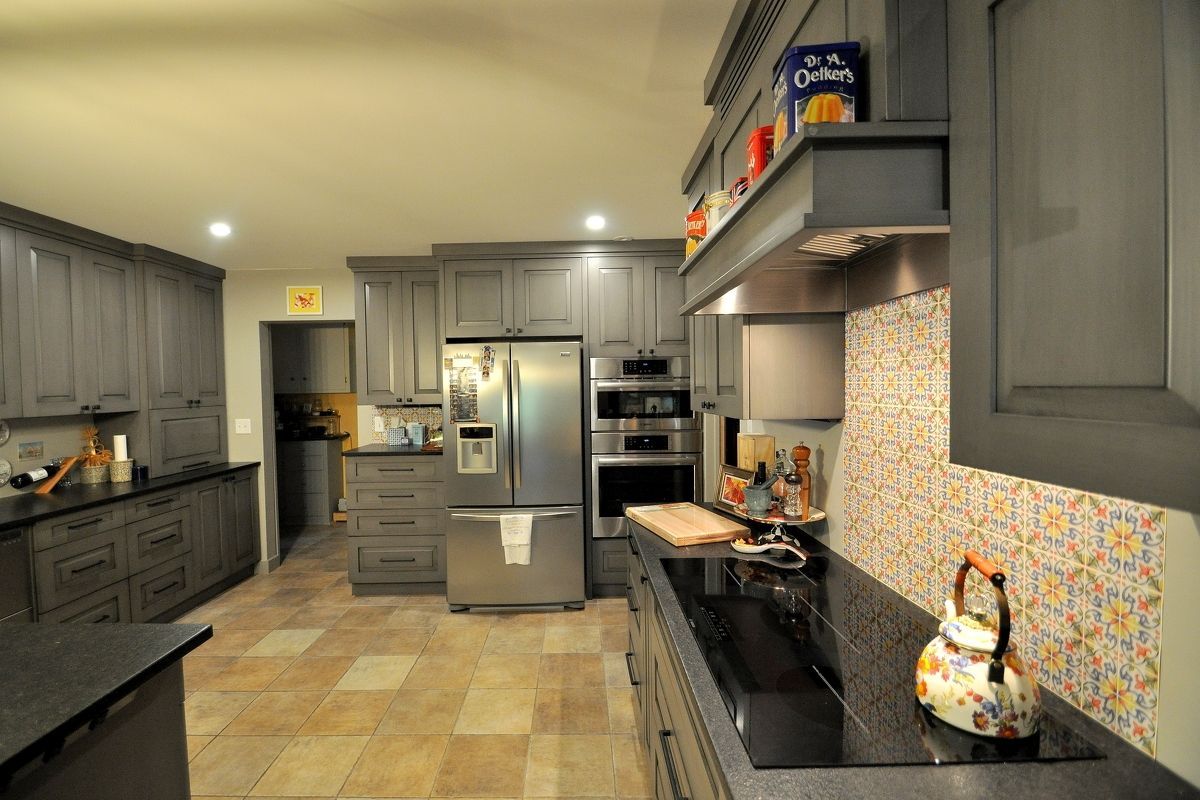Modern kitchen with gray cabinets, stainless steel appliances, black countertops, and patterned backsplash