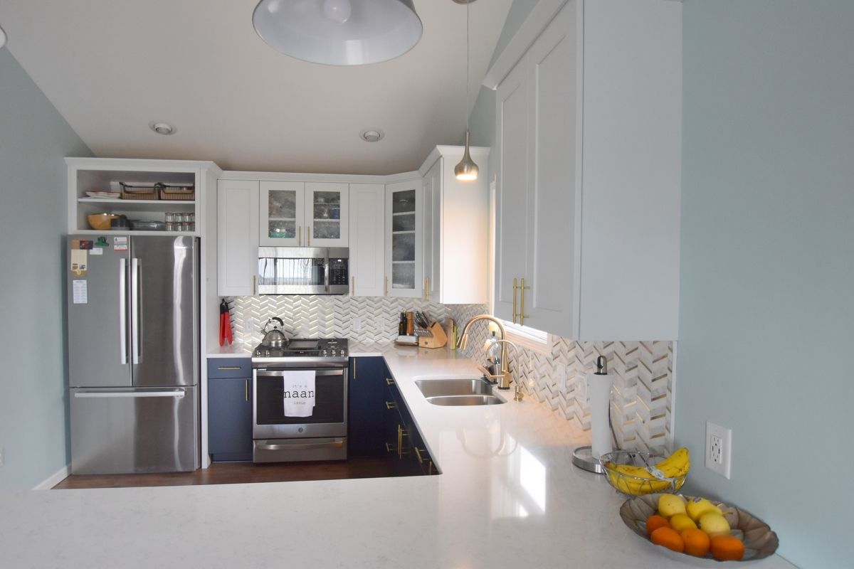Modern white kitchen with stainless steel fridge, black stove, and fruit bowl on a bright counter