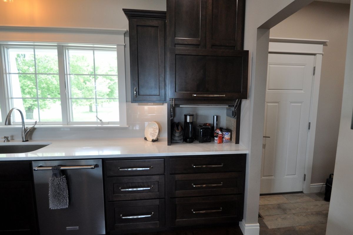 Modern kitchen with dark cabinets, stainless dishwasher, window sink, and open doorway