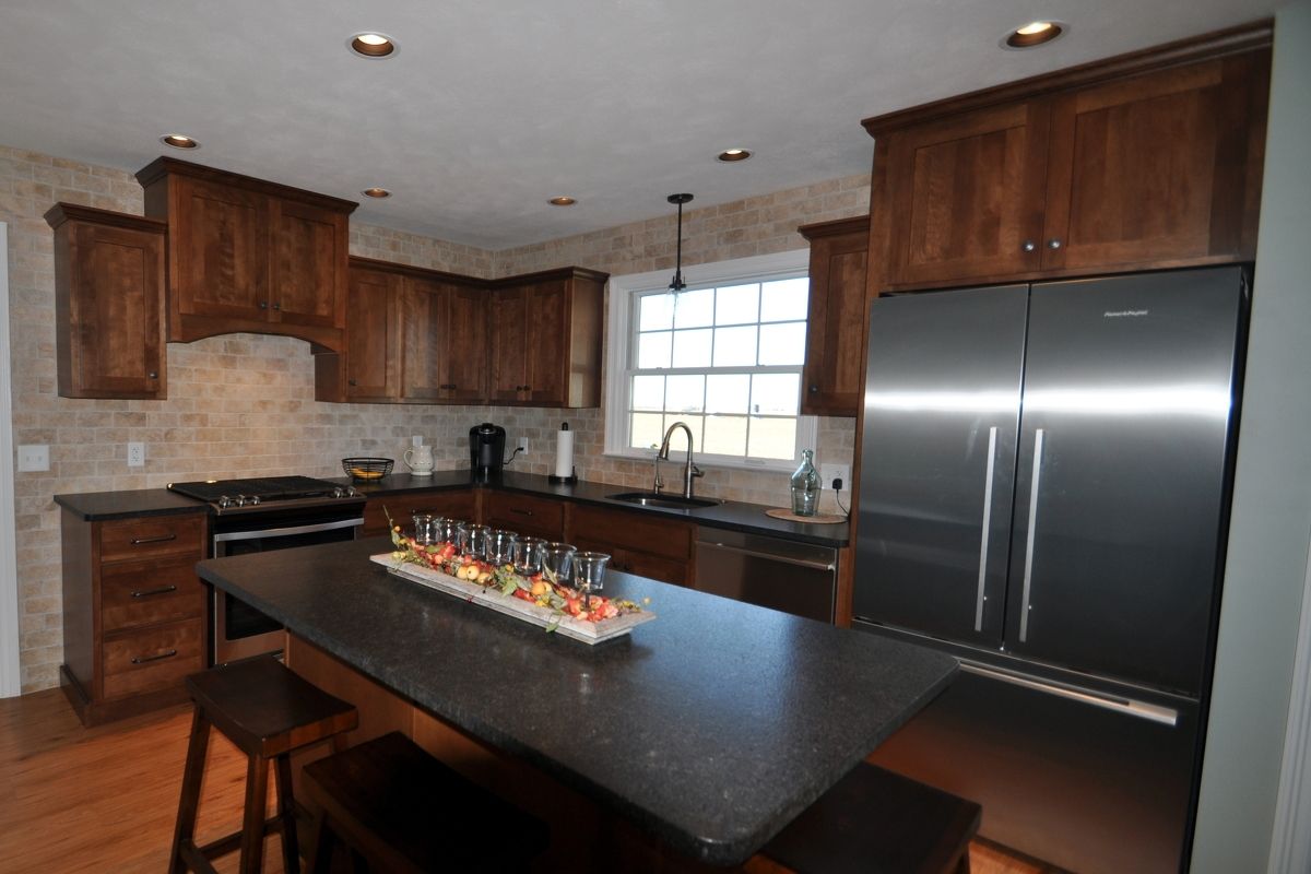 Modern kitchen with dark wood cabinets, stainless fridge, black island, and a tray of appetizers