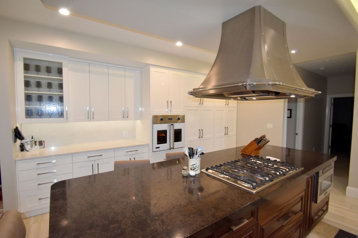 Modern kitchen with large island, stainless range hood, white cabinets, and dark granite countertops