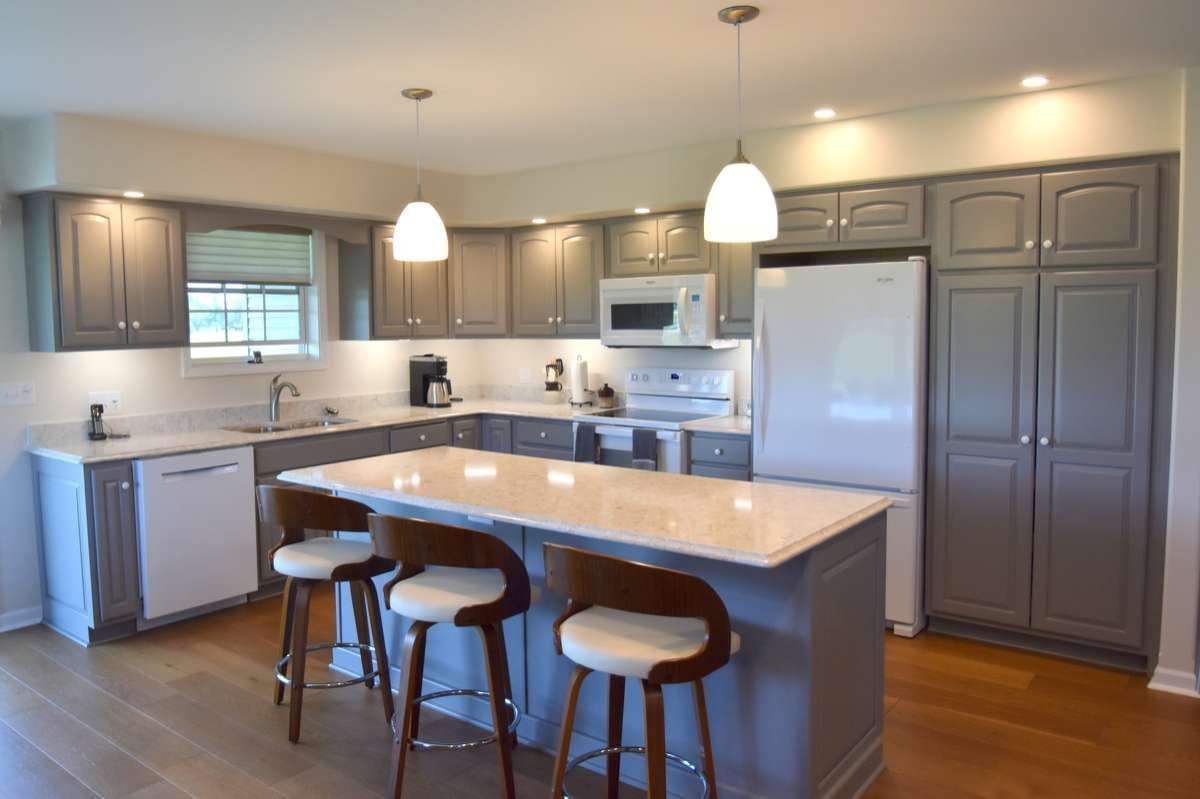 Modern kitchen with gray cabinets, white island, three stools, pendant lights, and stainless steel appliances