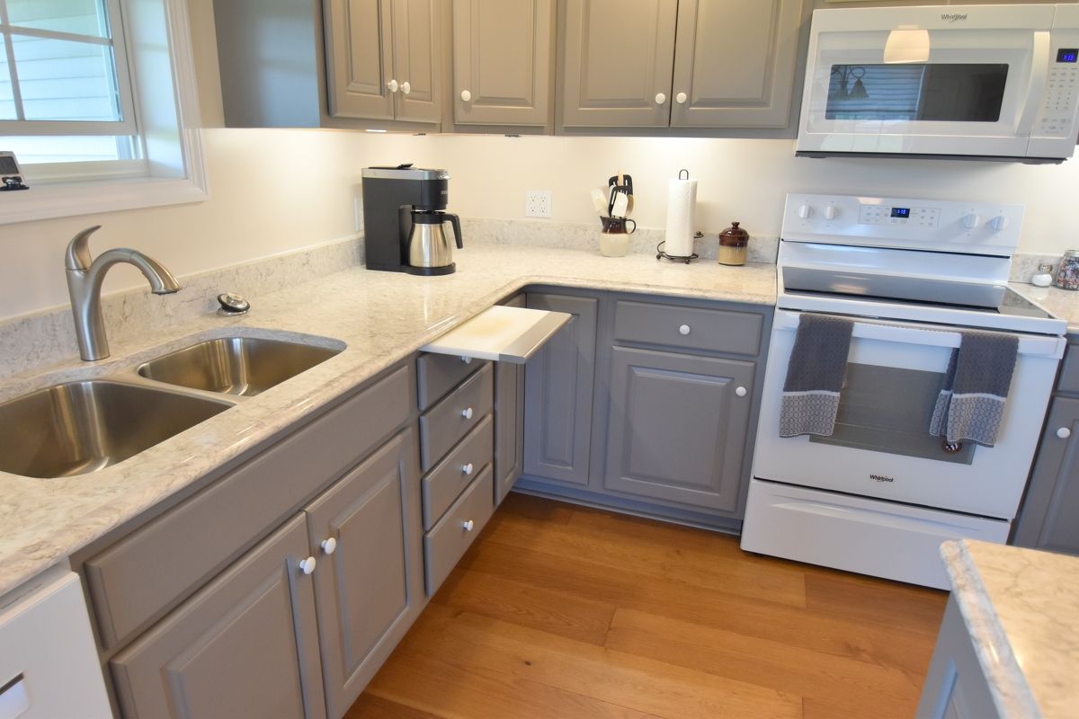 Bright kitchen with gray cabinets, white appliances, wooden floor, and double sink by a window