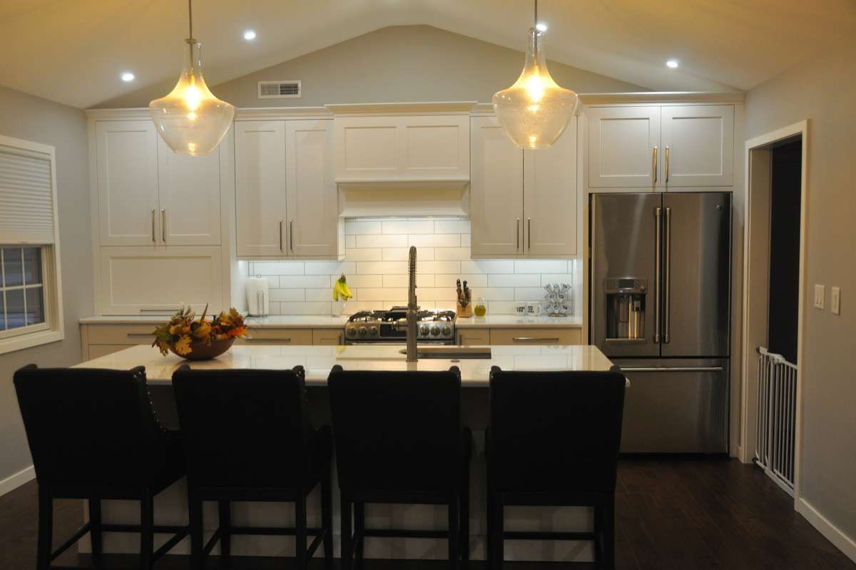 Modern kitchen with white cabinets, stainless steel appliances, dark island stools, and pendant lights