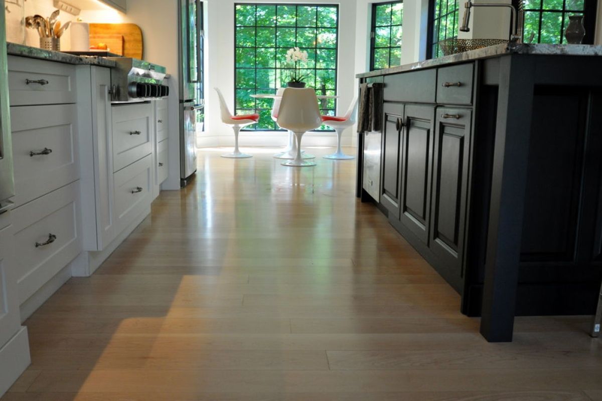 Modern kitchen with light wood floors, white cabinets, dark island, and a large window at the end.