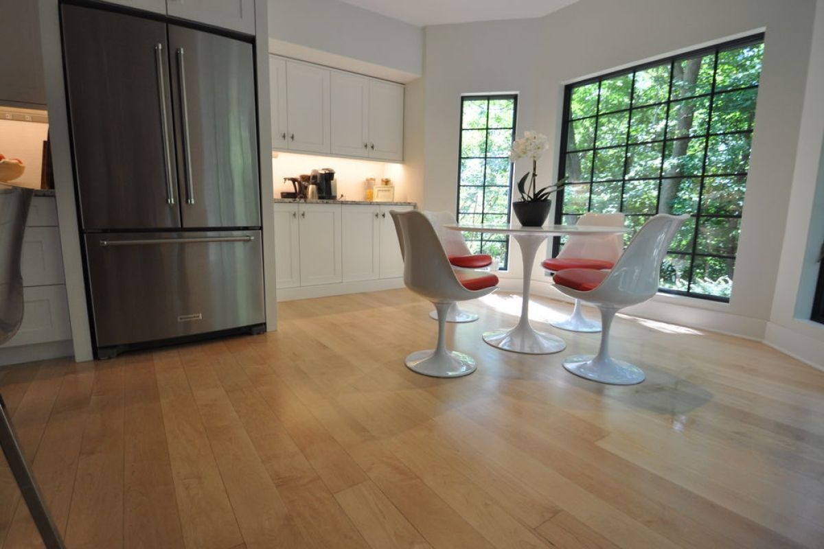 Modern kitchen with stainless refrigerator, white cabinets, round table, and large windows overlooking greenery