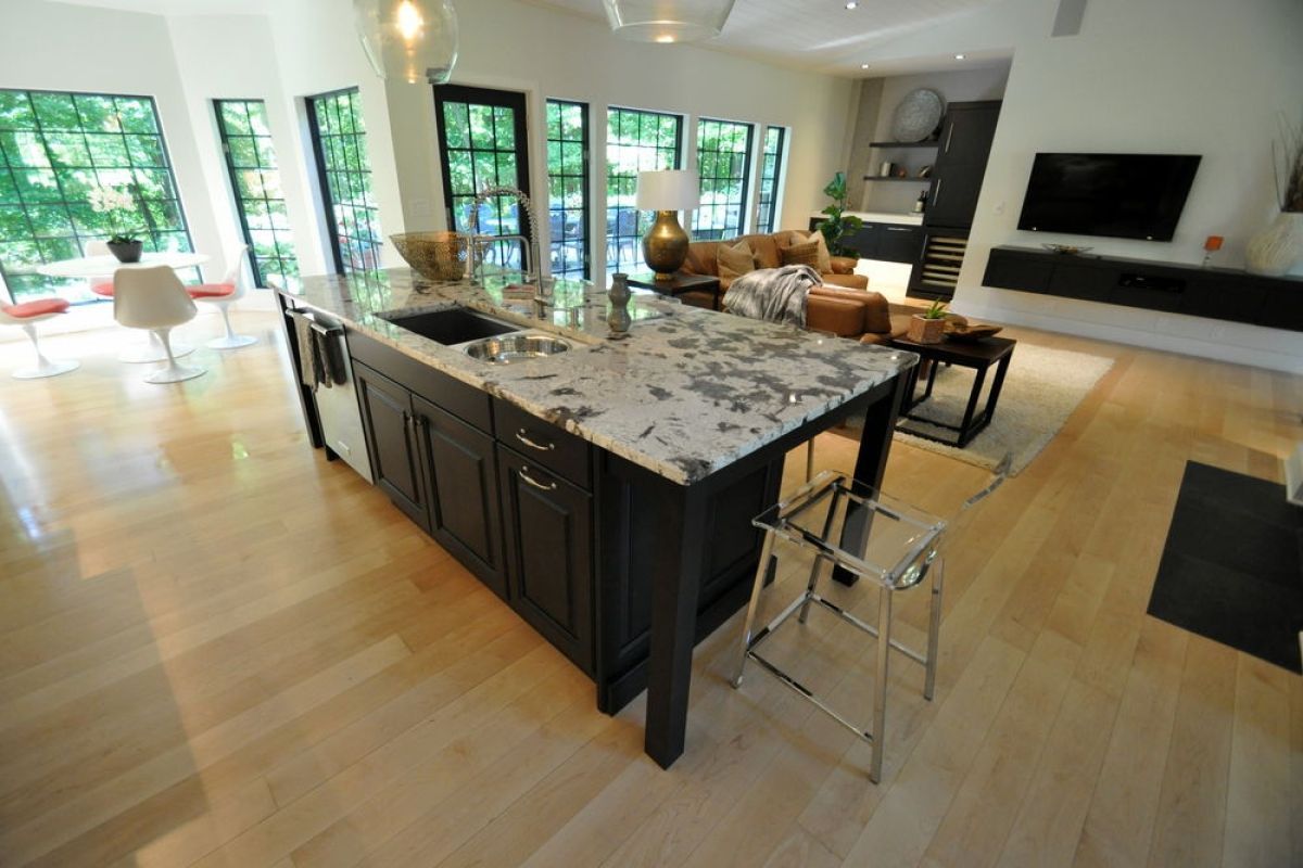 Modern kitchen with large island, dark cabinets, marble countertop, and open view to a bright living room