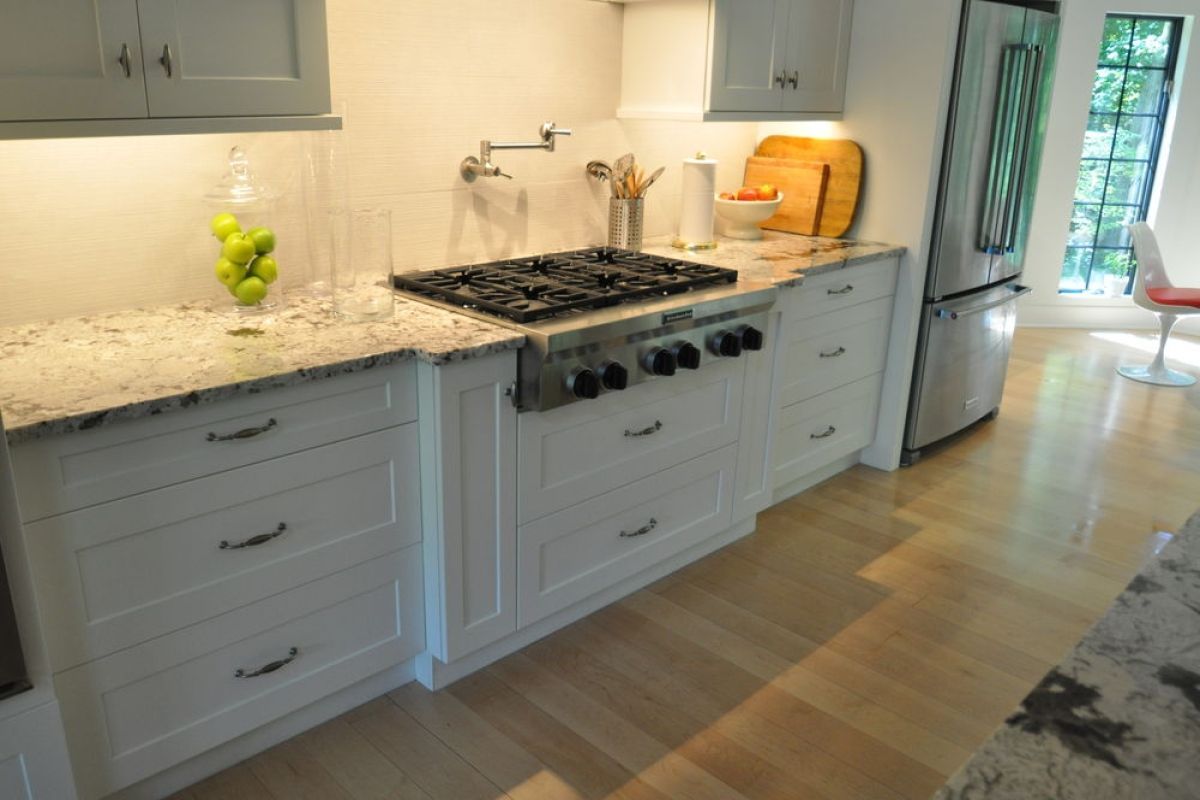 Bright modern kitchen with white cabinets, granite counters, gas range, and light wood floors