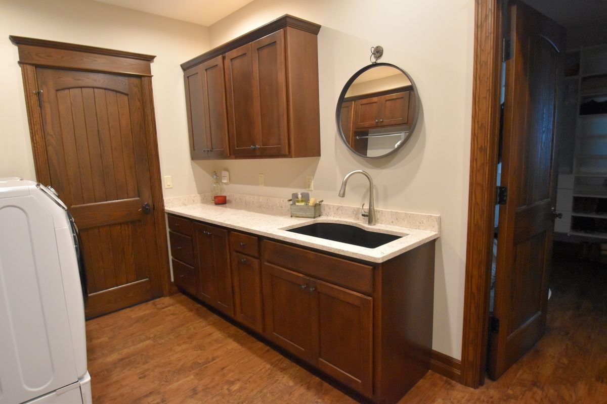 Laundry room with wood cabinets, sink, and round mirror beside a washer and doorway.