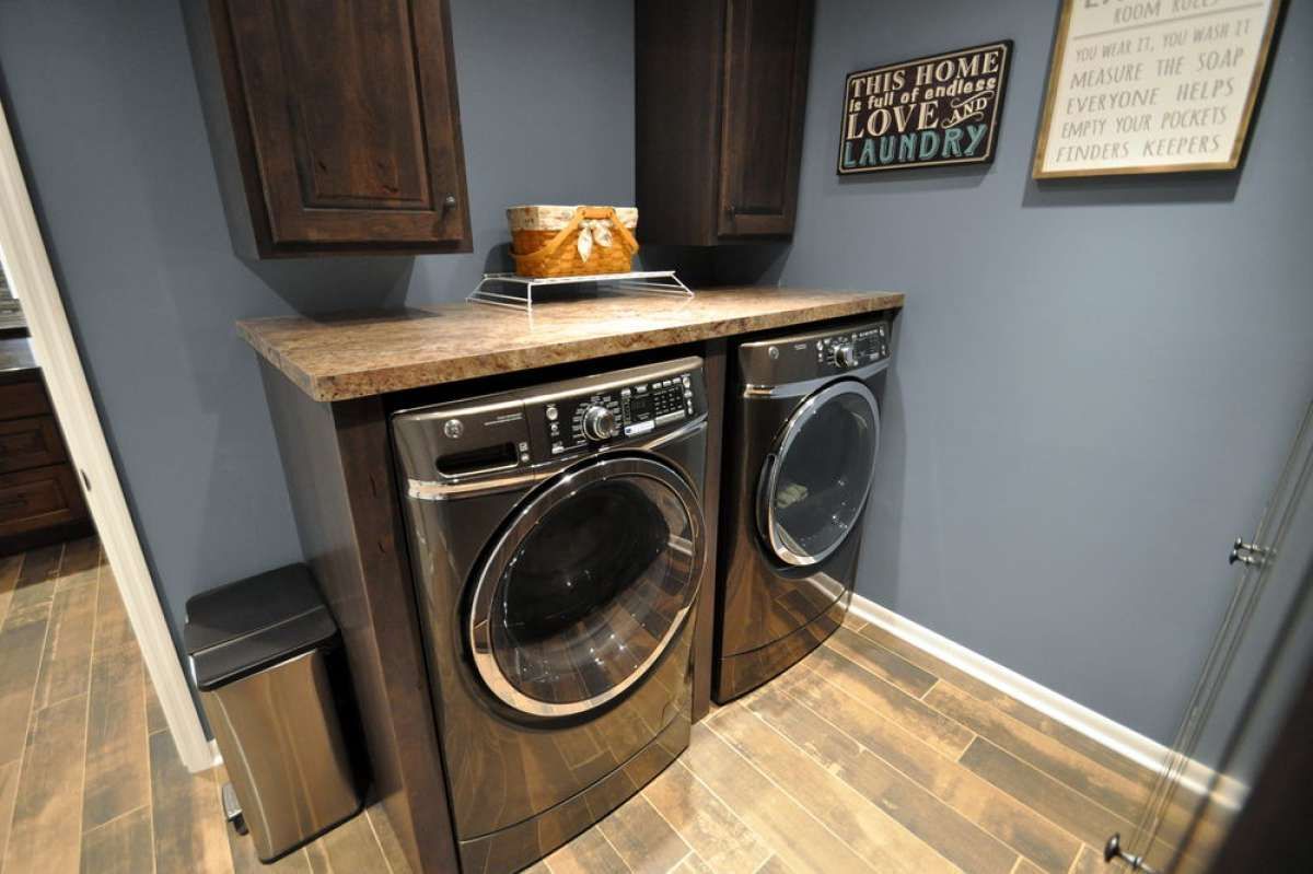 Black washer and dryer under a wood countertop in a small laundry nook with blue walls and tile floor