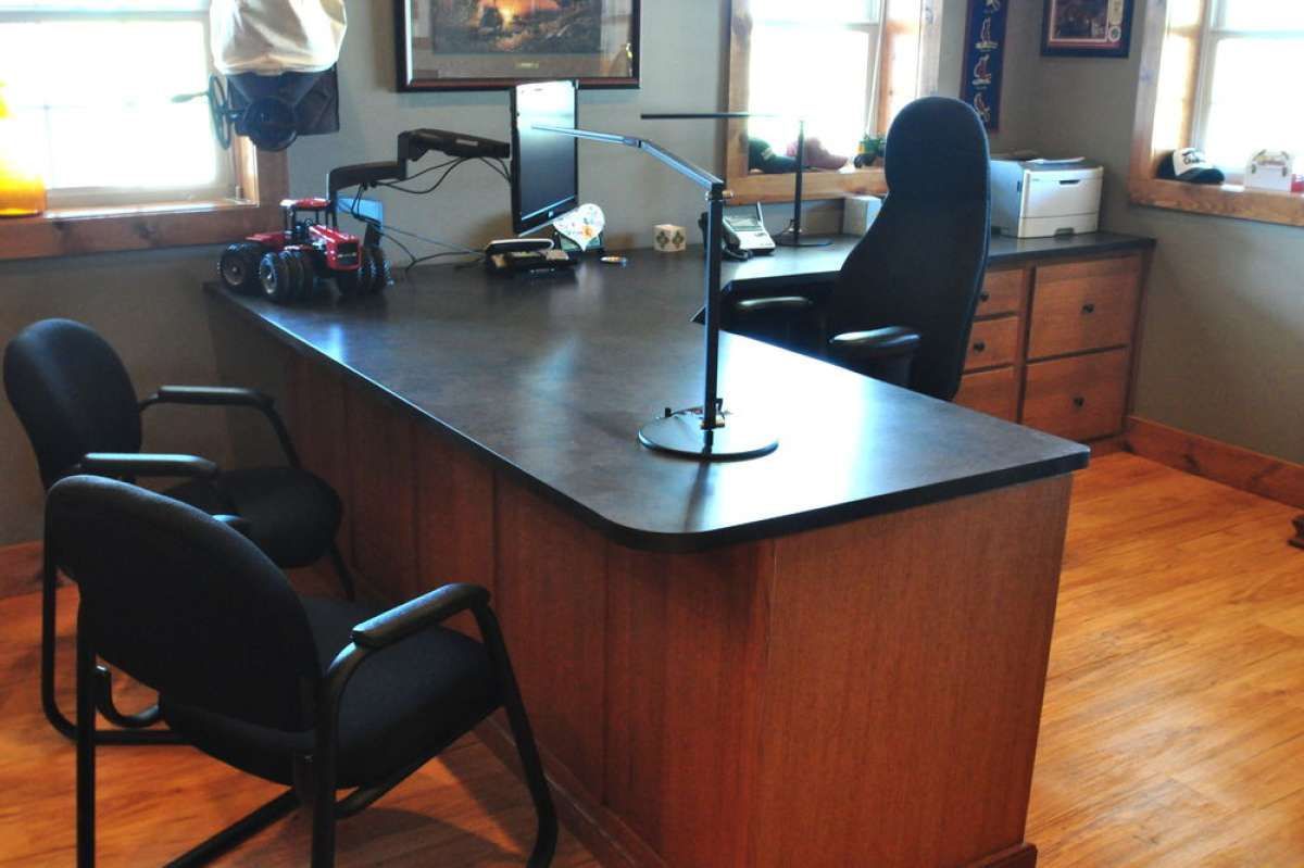 Office with large wooden desk, black chairs, computer equipment, and a window-lit hardwood floor.