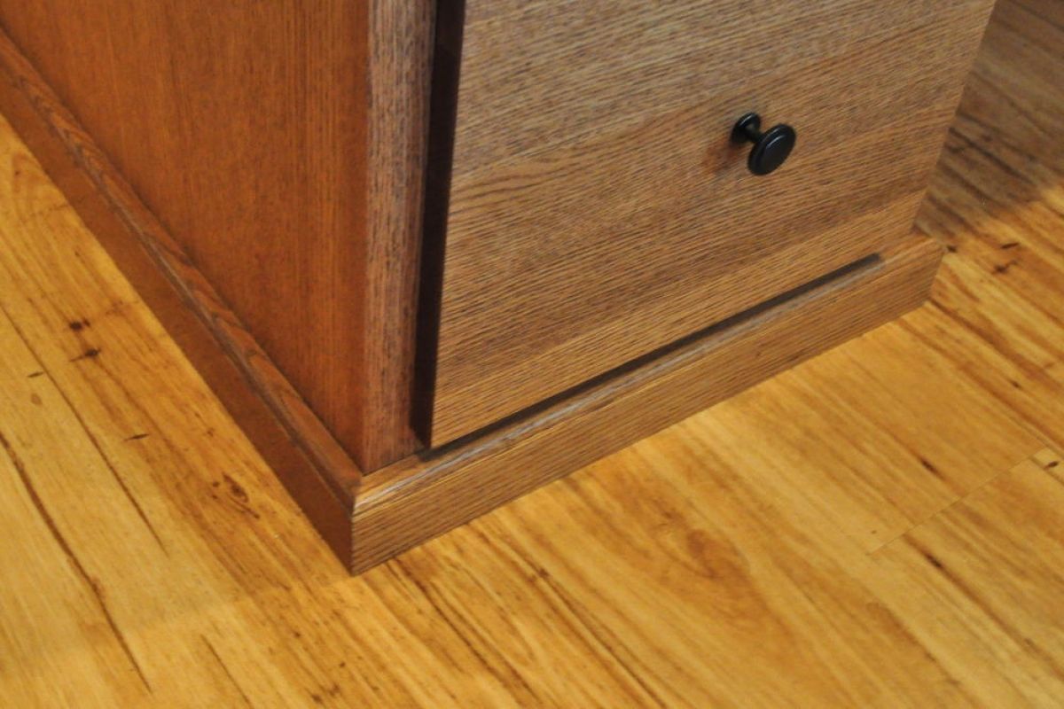 Wooden cabinet corner with a drawer and black knob on a hardwood floor