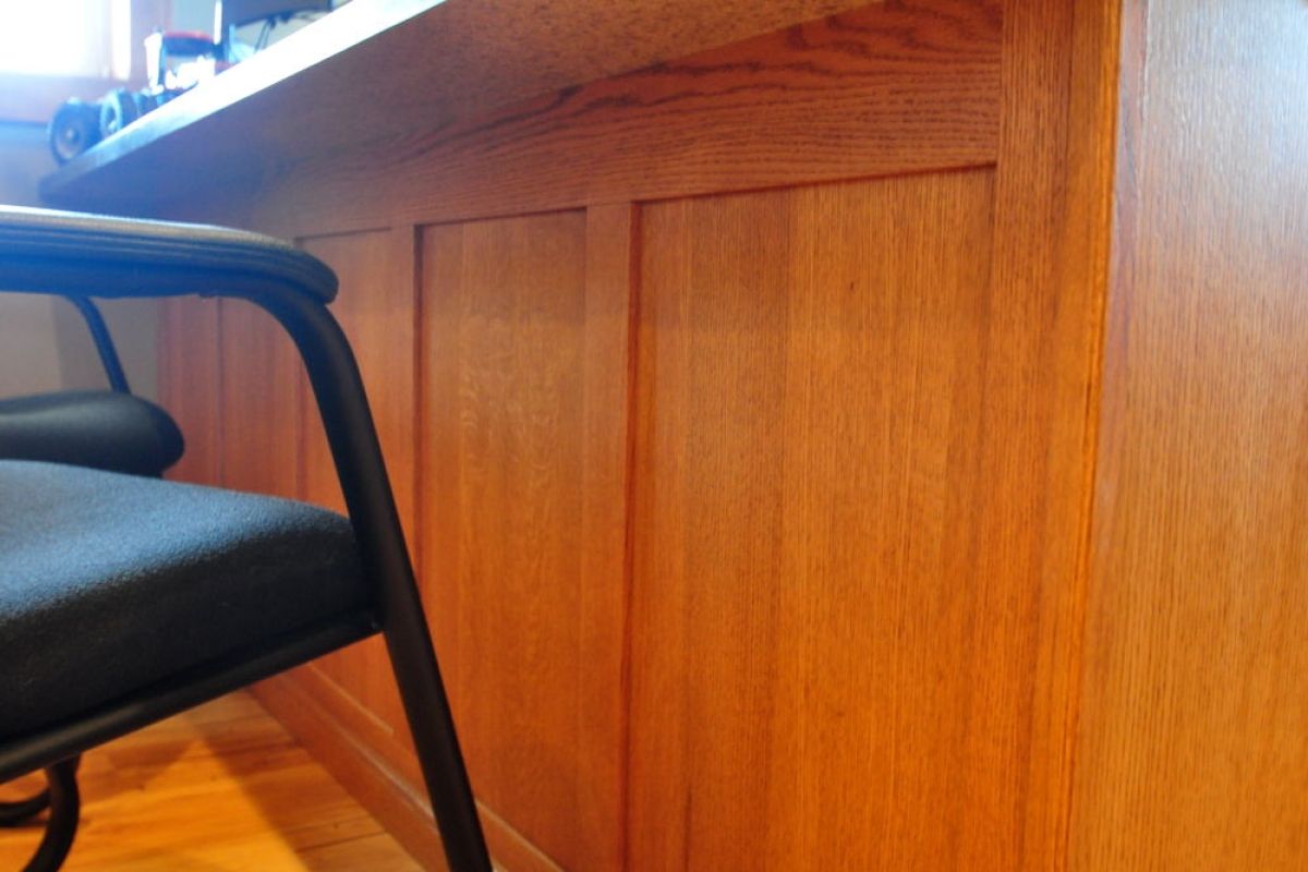 Black chair beside a wooden desk with paneled cabinet fronts and sunlight on the floor