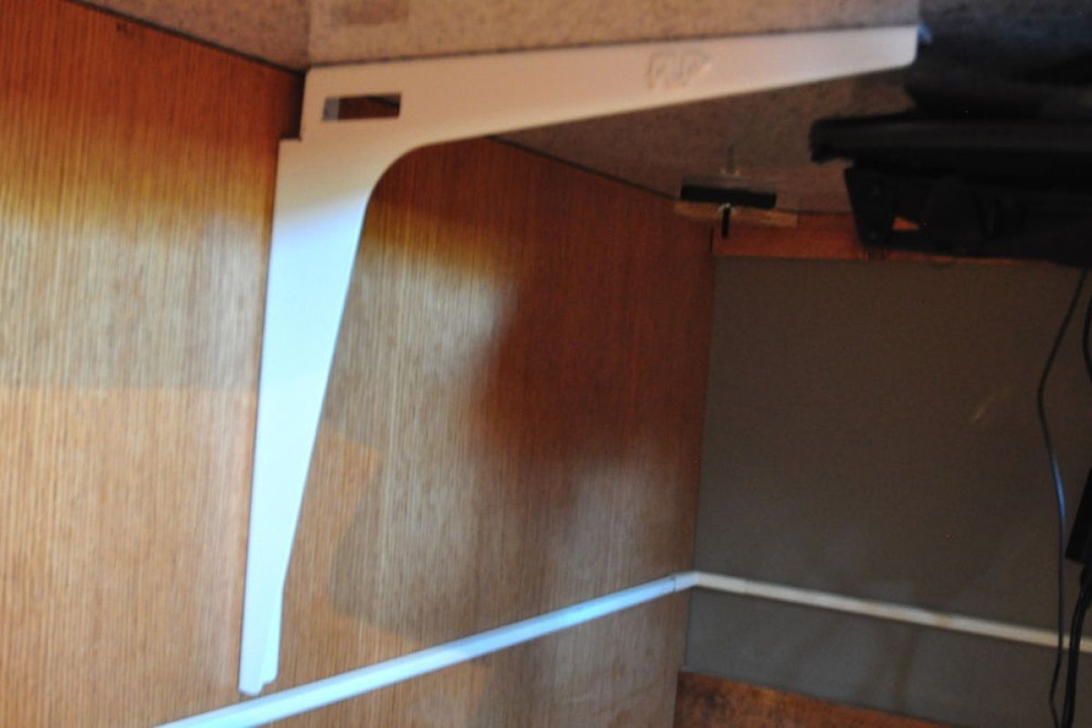 Under a wooden desk, a white metal leg and hanging cable are visible.