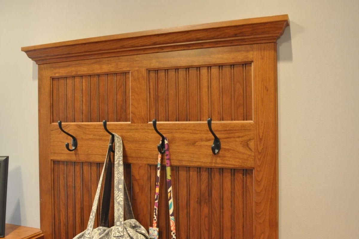 Wooden wall-mounted coat rack with four hooks and hanging bags against a beige wall