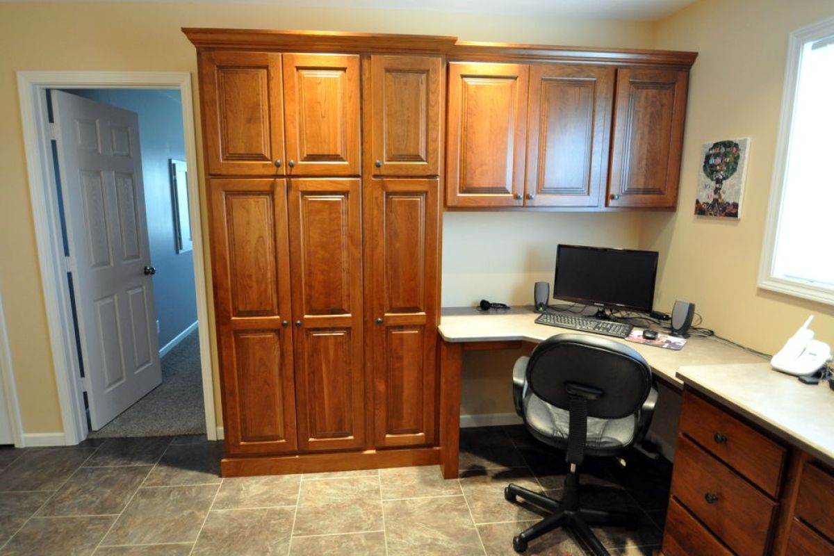 Home office with wooden cabinets, desk, computer, and office chair near a window
