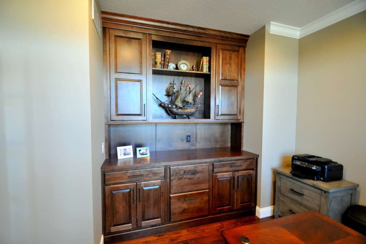 Wooden built-in cabinet with shelves and decor in a beige room, beside a small side table with a printer.