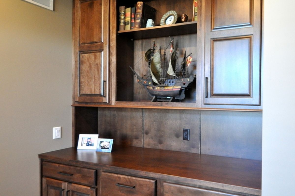 Built-in wooden desk and cabinets with decorative shelf display in a home office area