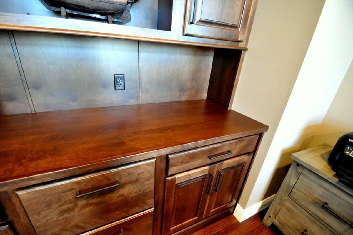 Wooden built-in desk with drawers, cabinets, and overhead shelves in a home interior.